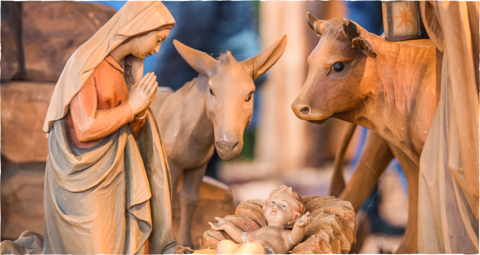 Holzgeschnitzte Weihnachtskrippe mit Maria, einem Esel und einem Ochsen, die sich über das  Jesuskind in der Krippe beugen 