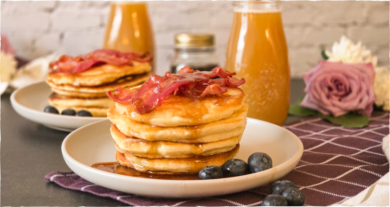Pancakes mit knusprigem Bacon und Weißbiersirup, dazu Blaubeeren; im Hintergrund Glas mit Weißbier-Mimosa – Kapuziner Weißbier