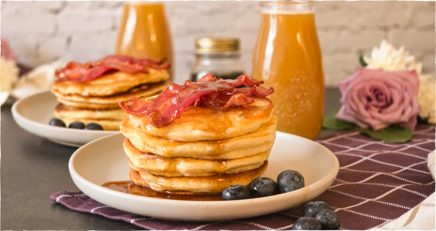 Pancakes mit knusprigem Bacon und Weißbiersirup, dazu Blaubeeren; im Hintergrund Glas mit Weißbier-Mimosa – Kapuziner Weißbier