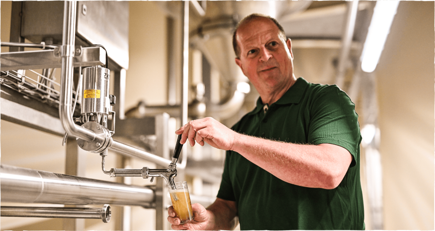 Braumeister zapft Probe aus einer Edelstahlleitung in der Brauerei, um die Qualität des Bieres zu prüfen