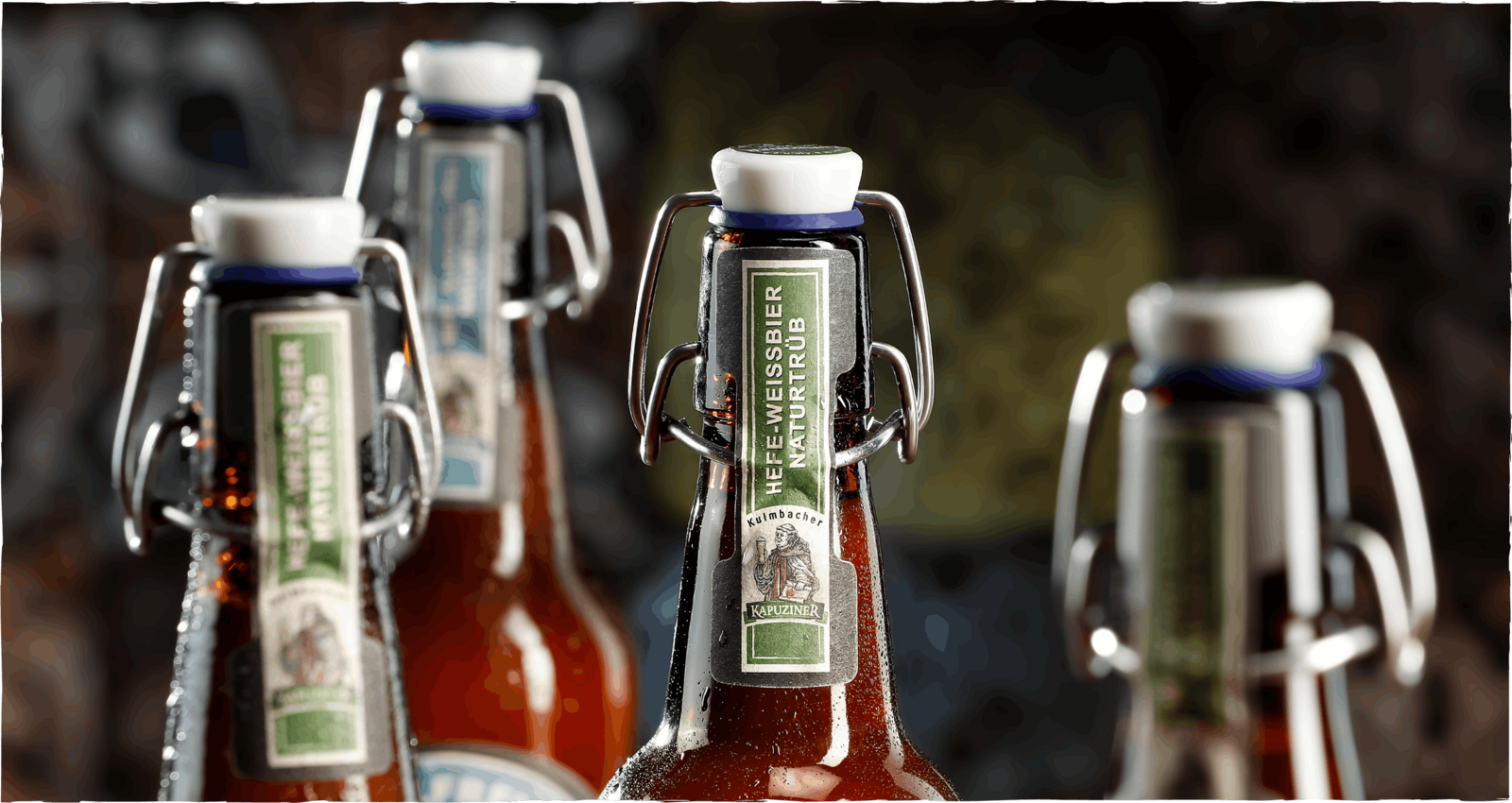 Kapuziner Weißbier Naturtrüb in Bügelflaschen mit Wassertropfen, warm ausgeleuchtet vor unscharfem Hintergrund in Brauerei-Atmosphäre.