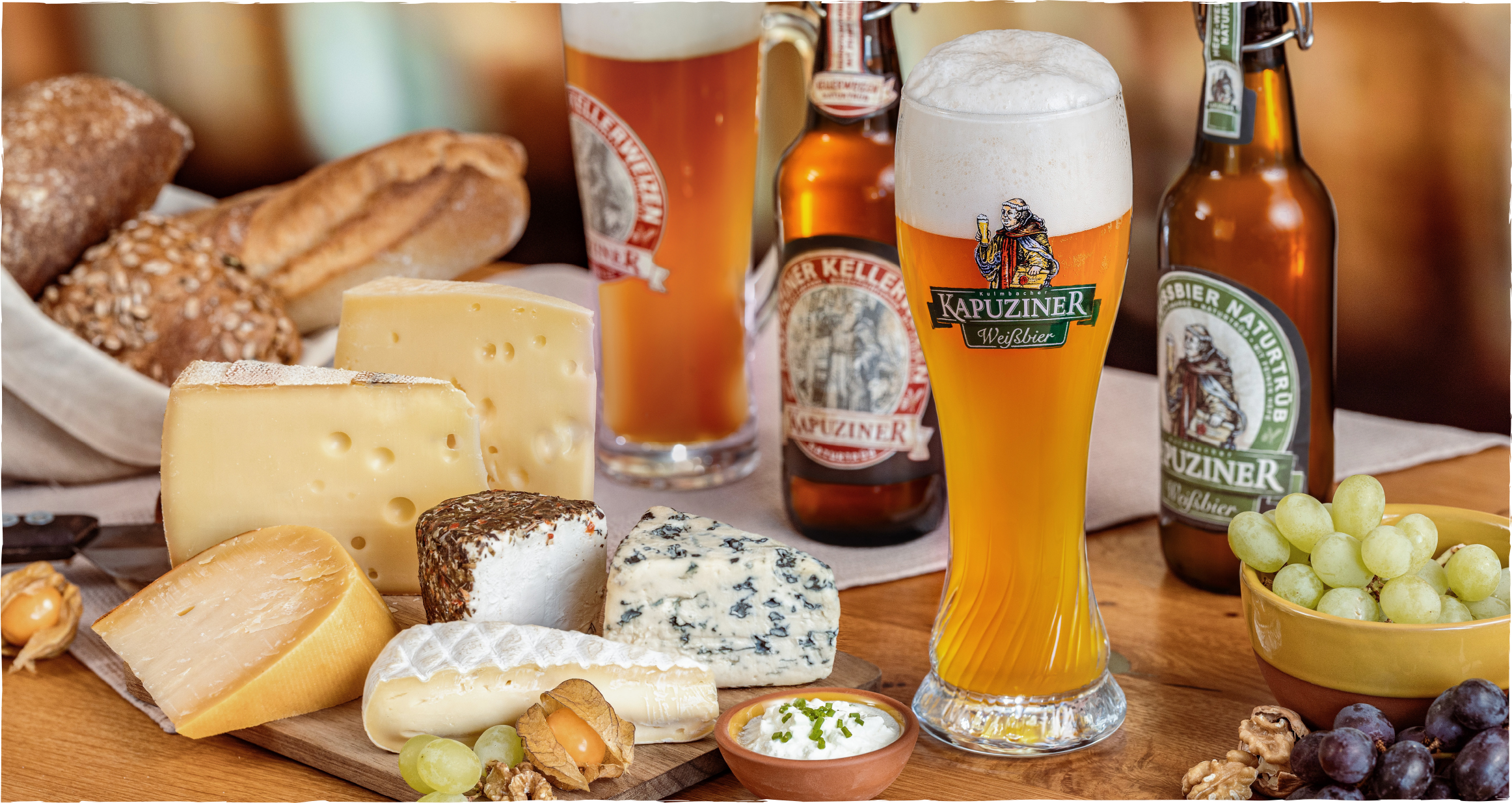 Kapuziner Weißbier, Käse, Trauben und Brot auf einem Holztisch arrangiert